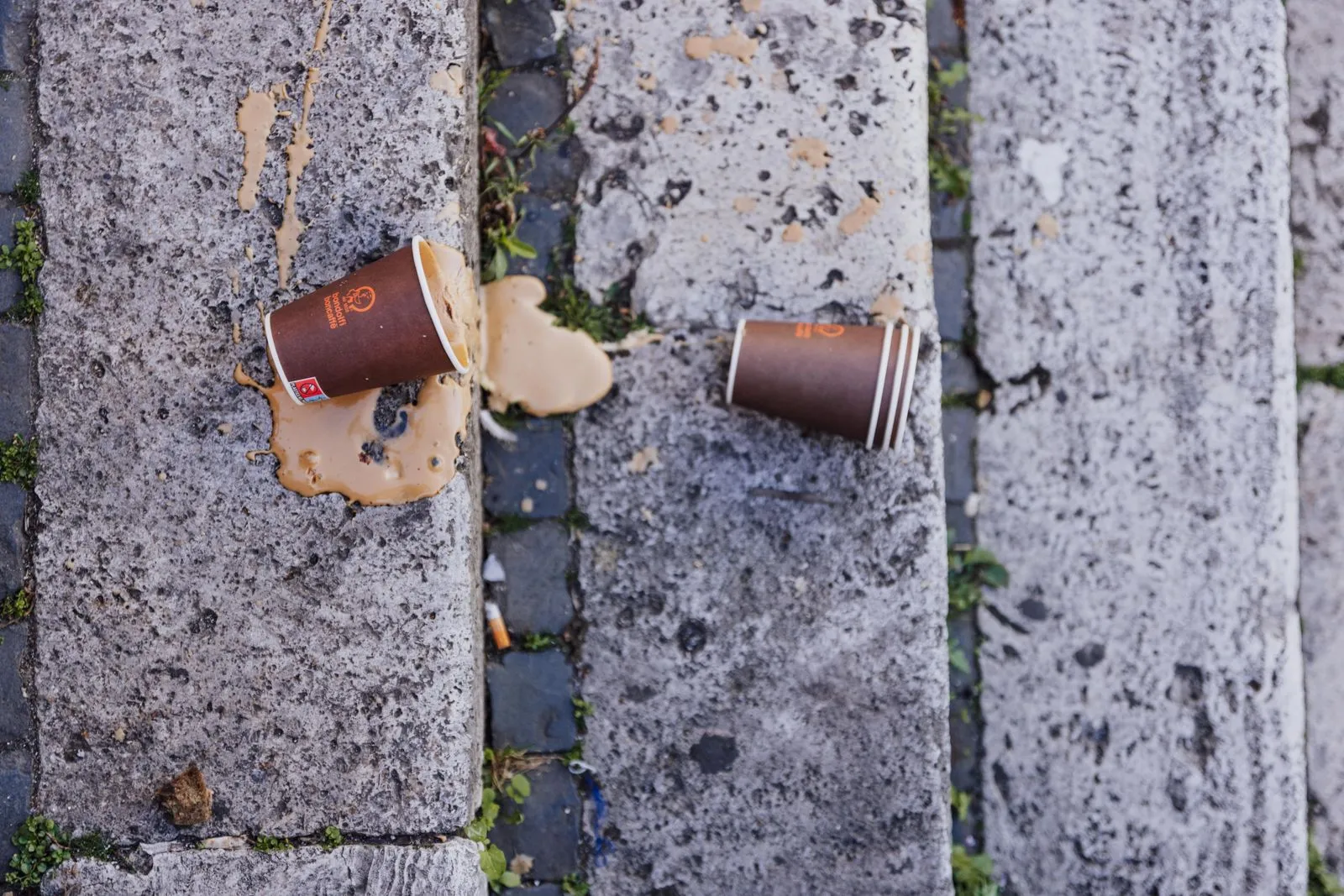 Aerial view of spilled coffee from paper cups on stone steps outdoors in daylight.